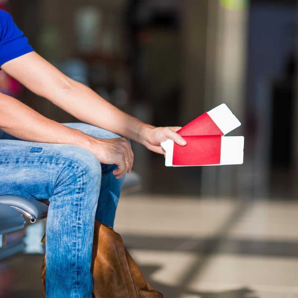 Person sitting in an airport holding red and white passport, symbolizing emergency passport services and travel readiness.