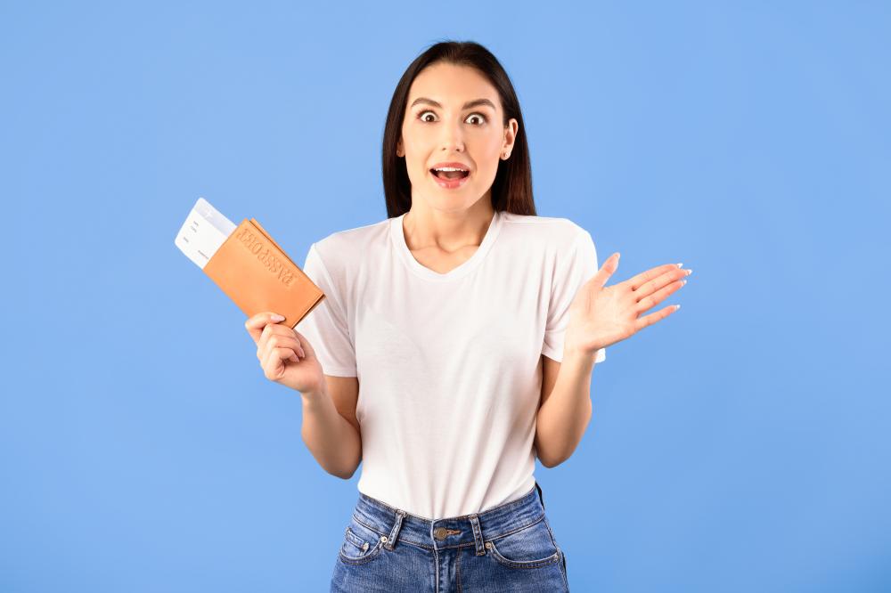 Surprised woman holding a passport and travel documents, expressing excitement, against a blue background, representing urgent passport services and travel readiness.